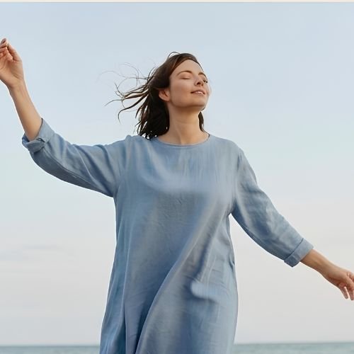 Mujer al aire libre frente al mar, con los ojos cerrados y los brazos abiertos, respirando